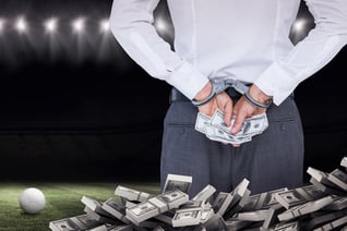 Businessman in handcuffs holding bribe against football pitch at night with ball and lights